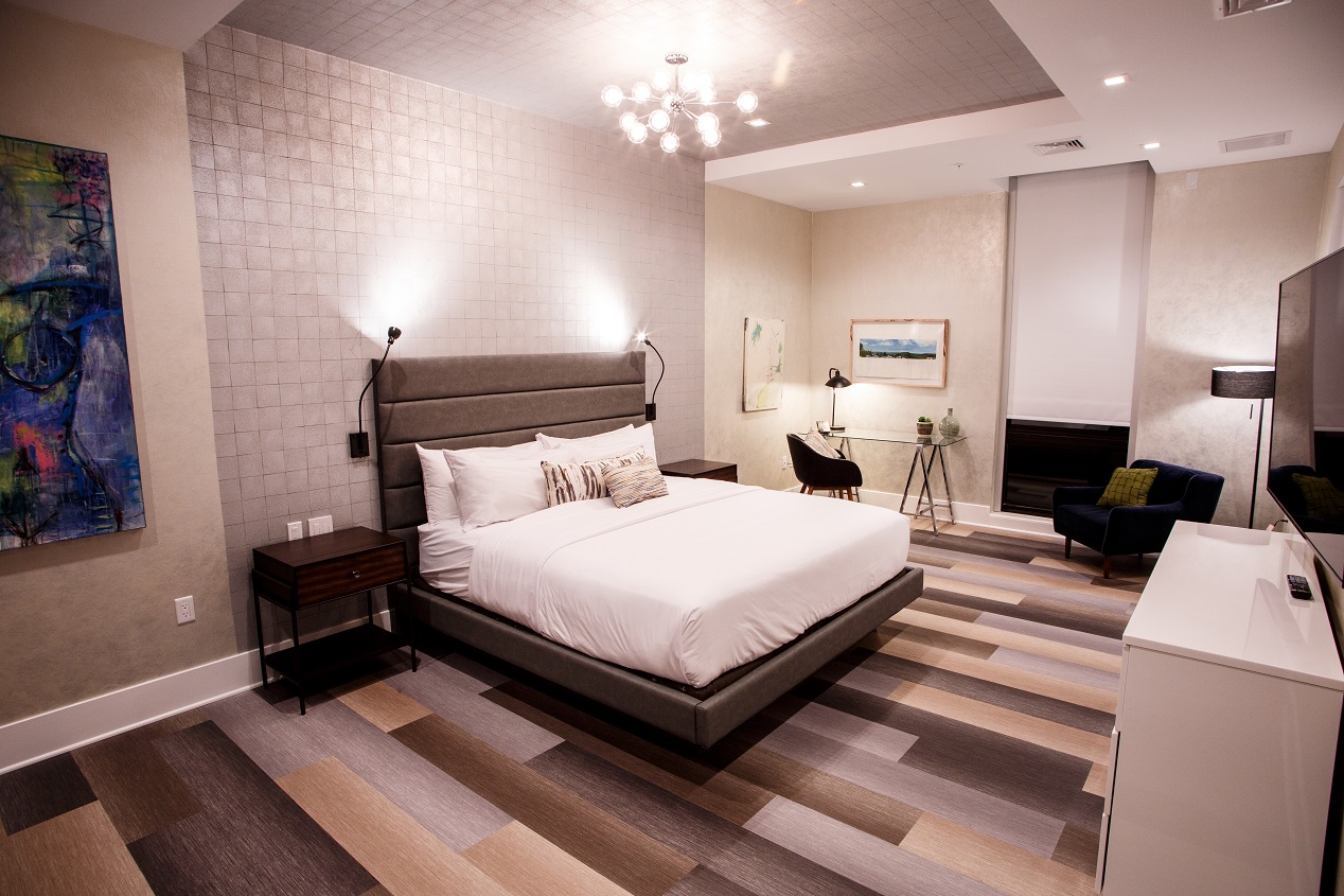 Bedroom in a penthouse suite with a white large bed, desk for work, loveseat and television